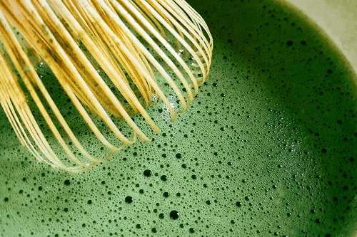 Close up matcha drink with a bamboo whisk on top of it
